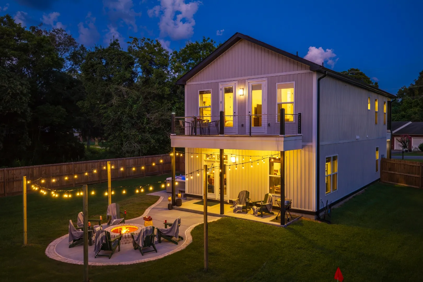 The rear of the Palmetto Haven House with its firepit, hot tub, string lights, and spacious lawn